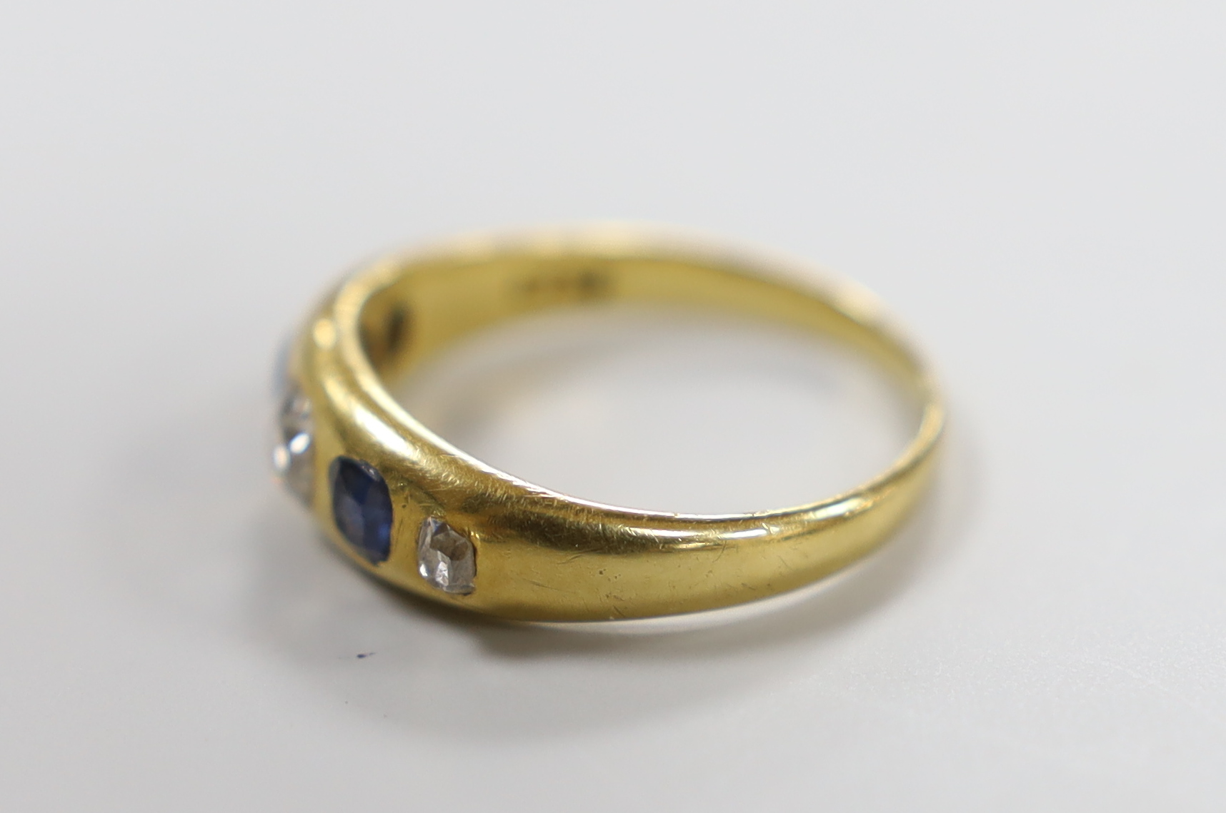 A yellow metal and gypsy set three stone diamond and two stone sapphire set half hoop ring, size S/T, gross weight 5.6 grams.